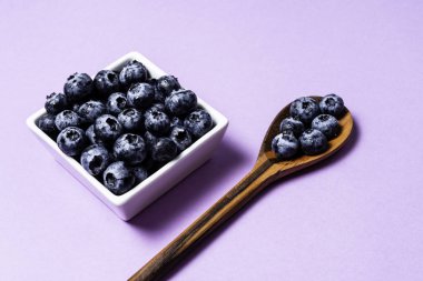 Mor arka plan ve tahta kaşık üzerinde pot içinde Taze yaban mersini