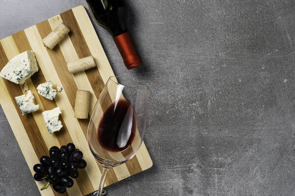 Полосатая доска с сыром и бокалом вина на бетонном фоне. Копировальное пространство
.