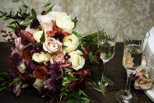 Bouquet of flowers on sweet table at wedding party. Glasses of champagne for the couple toast.