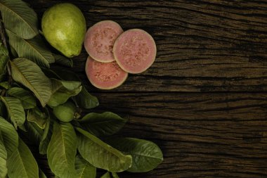 Tahta yıkım arka planında yeşil yapraklı taze kırmızı guavalar. Ağaç dokusu ve guava yaprakları..