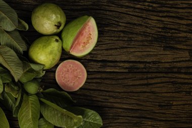 Tahta yıkım arka planında yeşil yapraklı taze kırmızı guavalar. Ağaç dokusu ve guava yaprakları..