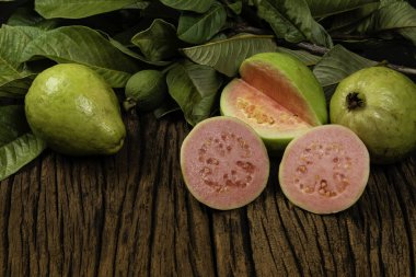 Tahta yıkım arka planında yeşil yapraklı taze kırmızı guavalar. Ağaç dokusu ve guava yaprakları..