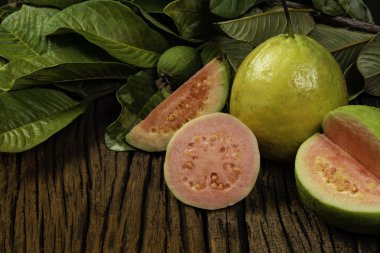 Tahta yıkım arka planında yeşil yapraklı taze kırmızı guavalar. Ağaç dokusu ve guava yaprakları..