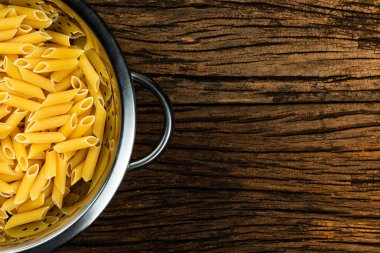 Eski ahşap arka plan üzerinde çiğ su süzgeci içinde yumurta ile makarna penne.