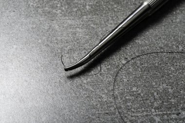 Dikiş ameliyatı için kavisli iğne tutucu. Beton arka planda naylon cerrahi iplik.