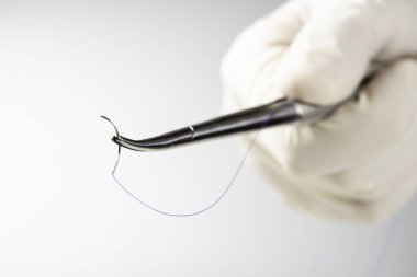 Doktor iğne tutucuyu beyaz arka planda tutuyor. Dikiş ipliği. Naylon cerrahi iplik.