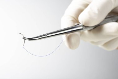 Doktor iğne tutucuyu beyaz arka planda tutuyor. Dikiş ipliği. Naylon cerrahi iplik.