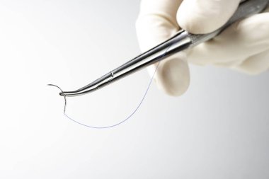 Doktor iğne tutucuyu beyaz arka planda tutuyor. Dikiş ipliği. Naylon cerrahi iplik.