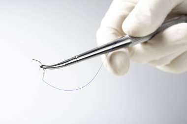 Doktor iğne tutucuyu beyaz arka planda tutuyor. Dikiş ipliği. Naylon cerrahi iplik.