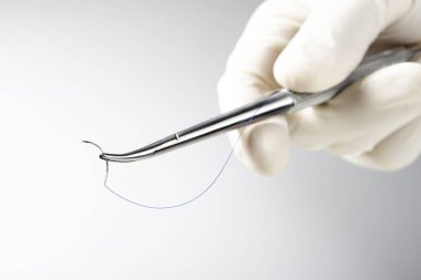 Doktor iğne tutucuyu beyaz arka planda tutuyor. Dikiş ipliği. Naylon cerrahi iplik.