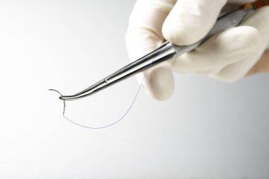 Doktor iğne tutucuyu beyaz arka planda tutuyor. Dikiş ipliği. Naylon cerrahi iplik.