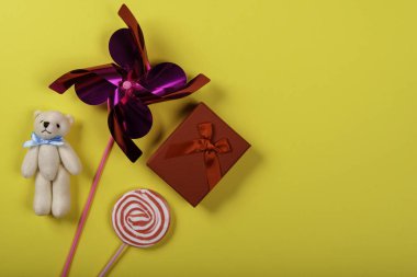 Fırıldak, oyuncak ayı, lolipop ve sarı arka plan üzerinde hediye. Resmin sağ tarafındaki metin için alan