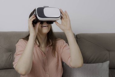 Vr kullanan kadın iki elinde yakışıklı tutarak kanepede oturan.