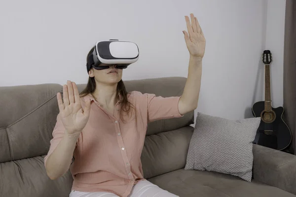 Woman using VR sitting on the couch with a sense of immersion in a virtual environment.