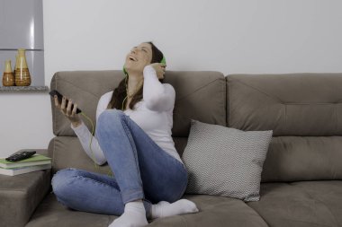 Güzel, genç kadın kanepede oturup müzik dinleyip şarkı söylüyor..