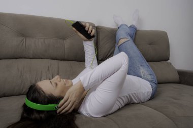 Kulaklıkla kanepede yatan genç güzel kız müzik dinleyerek ve ayakları yukarı ile rahatlatıcı.