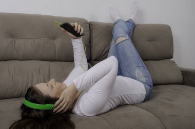 Kız evde kanepede müzik dinlemek.