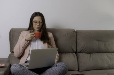Güzel kadın kanepede oturan çay içme ve dizüstü bilgisayar kullanarak.