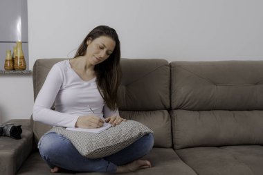 Güzel kadın kanepede otururken notlar yapıyor.