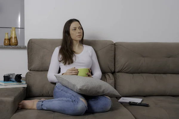 Młoda Ładna Kobieta Siedzi Kanapie Popijając Zupę Oglądanie Telewizji — Zdjęcie stockowe