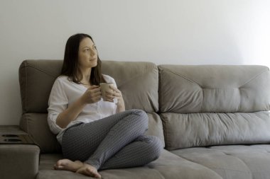 Pencere ışığı aydınlatıcı kadın kanepede oturmuş çay içiyor.