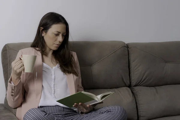 Businesswoman sitting on the couch having tea reading book. Space for text.