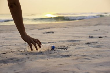 Kadın güneşin ışığının arka planında sahilde çöp topluyor. Deniz konsepti.