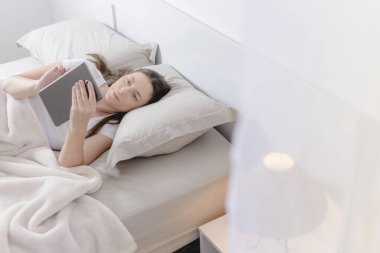 Yatakta uzanmış tablet üzerinde çalışan güzel bir kadın..