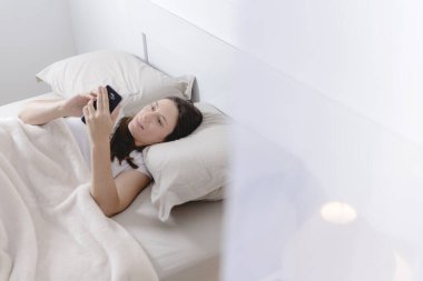 Yatakta uzanmış cep telefonuyla iş problemlerini çözen güzel bir kadın..