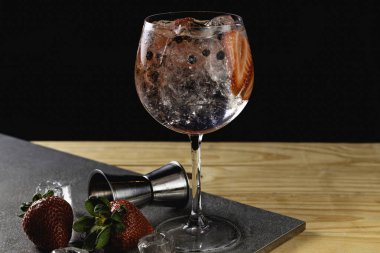 Gin tonic strawberry with juniper stone background in gray color.