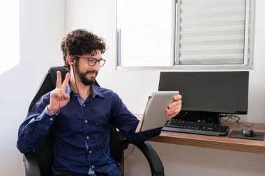 Ofisinde video araması yapmak için tablet kullanan yakışıklı bir İspanyol..