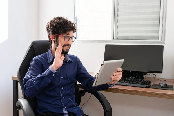 Latin man in his office using tablet to make video call. Home office concept.