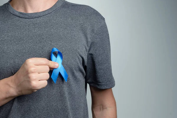 Man putting dark blue ribbon on his shirt. Awareness symbol.