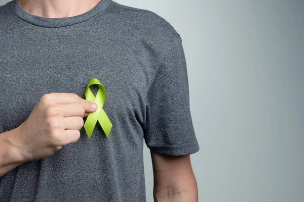 Man putting turquoise or teal ribbon on his shirt. Awareness symbol.