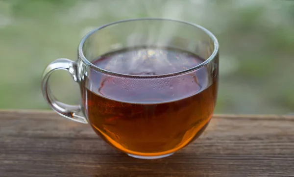 Transparent cup of black hot tea on a wooden table on a background of nature