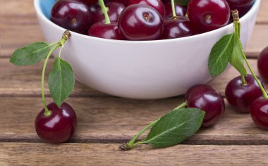 Olgun kiraz ahşap masa yakın çekim yeşil yaprakları ile beyaz tabak