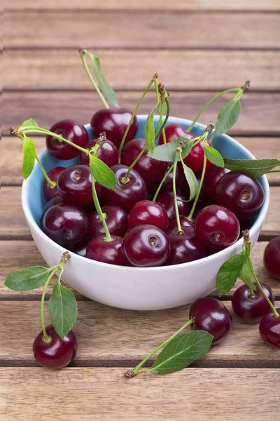 Olgun kiraz ahşap masa yakın çekim yeşil yaprakları ile beyaz tabak