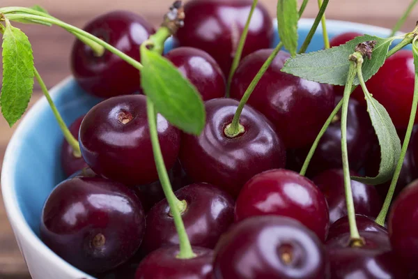 Olgun kiraz ahşap masa yakın çekim yeşil yaprakları ile beyaz tabak