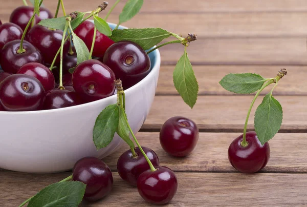 Olgun kiraz ahşap masa yakın çekim yeşil yaprakları ile beyaz tabak