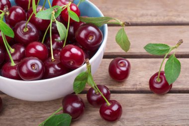 Olgun kiraz ahşap masa yakın çekim yeşil yaprakları ile beyaz tabak