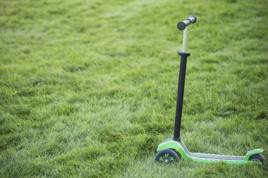 3 tekerlekli çocuk Yeşil scooter içinde sulu çim yakın çekim, önden görünüm