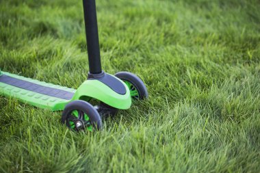 3 tekerlekli çocuk Yeşil scooter içinde sulu çim yakın çekim, önden görünüm