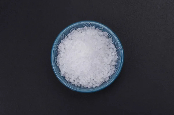 天然海水加碘盐在一个蓝色传统的小碗在黑色背景 顶部视图 — 图库照片