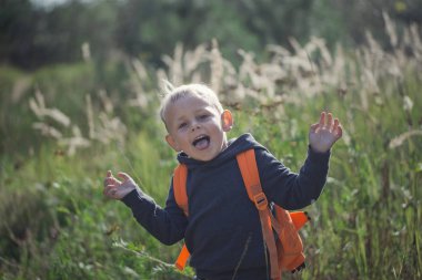 Bir yaz güneşli da bir orman yolu boyunca mutlu küçük bir çocuk bir sırt çantası ile çalışır