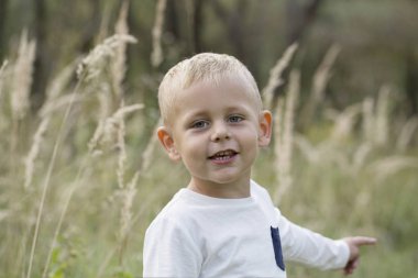 Küçük sarışın çocuk bakarak bir alanda yüksek kuru ot kamerada bir orman arka plan üzerinde güneşli bir günde