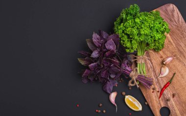 Bir avuç taze maydanoz ve kırmızı fesleğen fiyonk ve baharat ve sarımsak bir kara tahta, üstten görünüm üzerinde bir karışımı ile bir ip ile sargılı