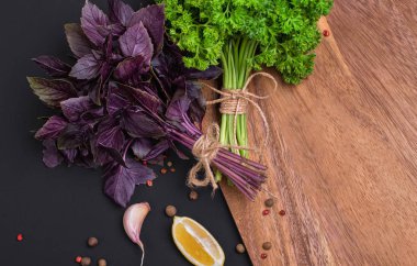 Bir avuç taze maydanoz ve kırmızı fesleğen fiyonk ve baharat ve sarımsak bir kara tahta, üstten görünüm üzerinde bir karışımı ile bir ip ile sargılı