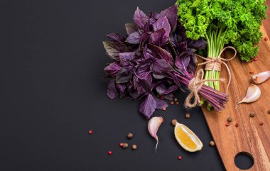 Bir avuç taze maydanoz ve kırmızı fesleğen fiyonk ve baharat ve sarımsak bir kara tahta, üstten görünüm üzerinde bir karışımı ile bir ip ile sargılı