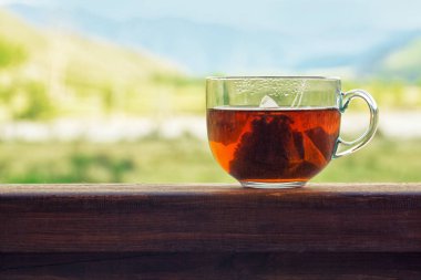 Doğa panorama arka plan üzerinde üçgen siyah çay poşeti ile şeffaf kupa