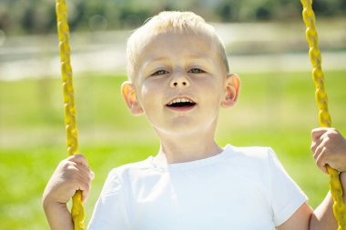 Küçük çocuk kameraya bakar ve Bahçesi Şehir parkta salıncağa bir güneşli yaz gününde sahiptir yakın çekim